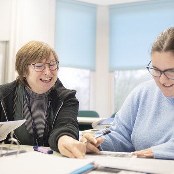 A student and teacher sit at a table, looking at some work together.