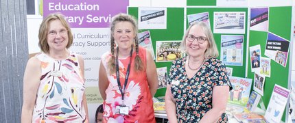 Three ELS librarians smile at the camera and stand in front of an ELS display