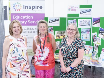 Three ELS librarians smile at the camera and stand in front of an ELS display