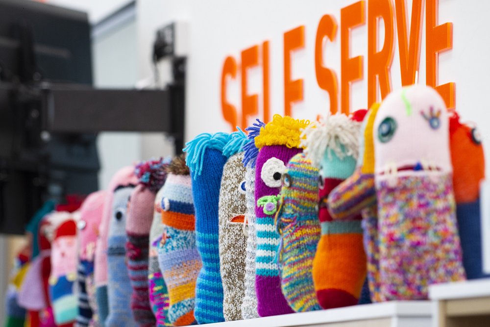 A row of knitted worry monsters on a library shelf