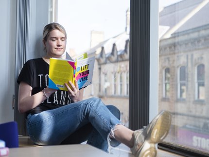 Blonde woman sitting by a window reading a book
