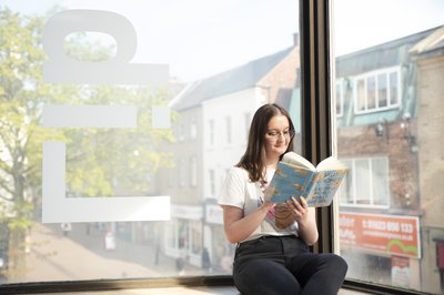 A woman reading a Sally Rooney book while perched on a windowsill