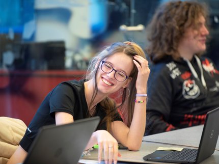 An Inspire College student leaning on her desk with a laptop in front of her, laughing with another student.