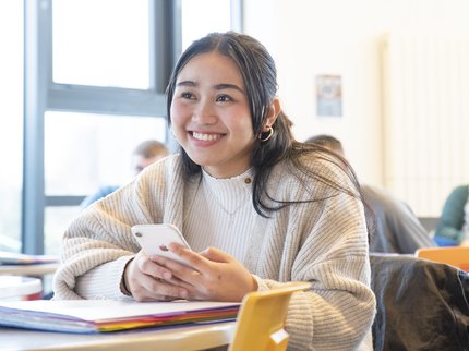 College learner smiling, looking up from her phone at a desk.