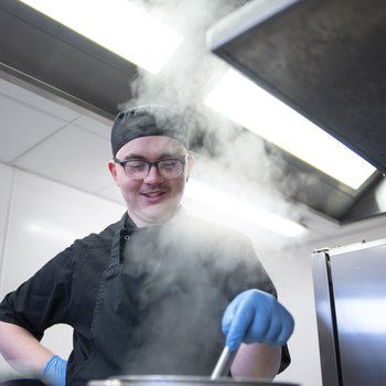 A young person cooking in a professional kitchen.