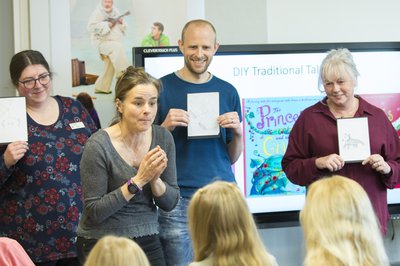 four people stand at the front of a presentation holding books