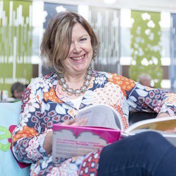 A woman smiling as she reads a children's book.