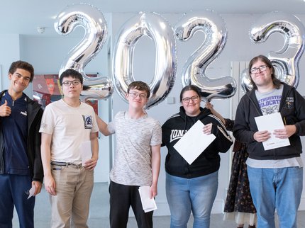 Inspire College learners pose with their GCSE results in front of balloons spelling 2023.