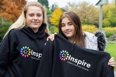 Two female students holding up black Inspire learning hooded jumpers