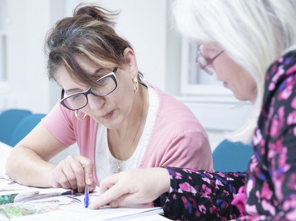 A woman wearing pink looking at written text with a tutor.