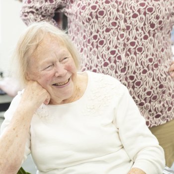 A mature woman wearing a white top smiling at someone out of picture.