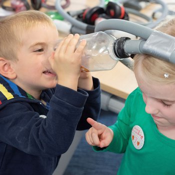 A young boy and girl experimenting with science tricks using household equipment including plastic bottles.