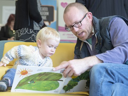 A parent reads a book with a green leaf on the cover to their child