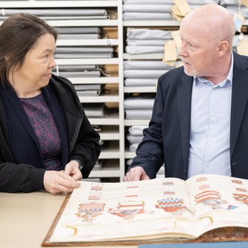 Adult female and male looking at archival documents at a table