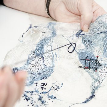 Close up photo of artists hand pulling a stitch through some of her fabric artwork