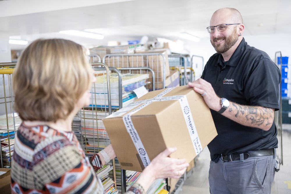A woman in a blue jumper hands over a book to a customer