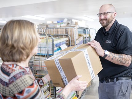A member of the distribution team hands over a carboard box full of books to school staff