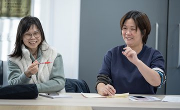 Two east asian learners enjoying their ESOL course with Inspire Learning laugh and smile together during their course.