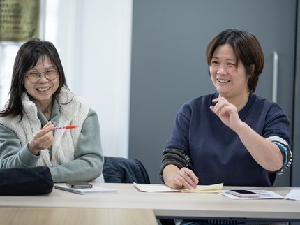Two east asian learners enjoying their ESOL course with Inspire Learning laugh and smile together during their course.