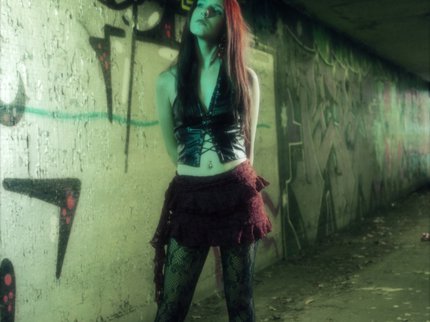 A young woman with long dark hair stood against a wall of graffiti, wearing black tights and boots with a red skirt.