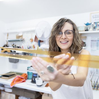 Glass maker Emma is holding up two pieces of orange glass in front of the camera. She is smiling and wearing glasses.