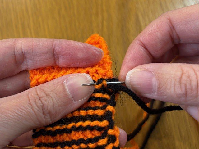 Stitching a thread of excess yarn onto the back of a knitting project