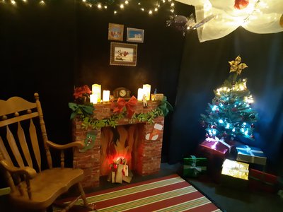 An image of a grotto, set up around a brick effect fire place with a Christmas tree in one corner and a wooden rocking chair in another