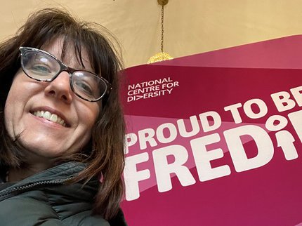 Inspire Youth Arts Manager Rebecca Streets pictured in front of a pink proud to be FREDiE banner at the National Centre for Diversity Conference
