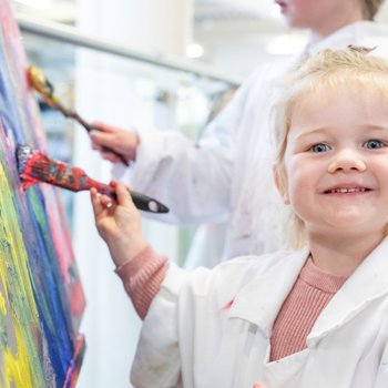 little girl painting at an easel, smiling