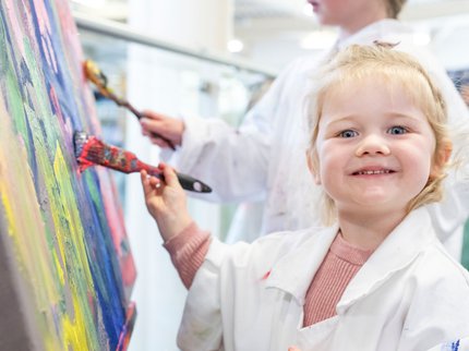 little girl painting at an easel, smiling