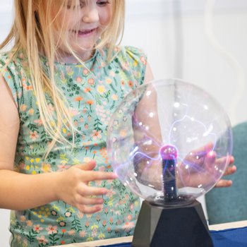 A girl holding her hands over a giant plasma ball.