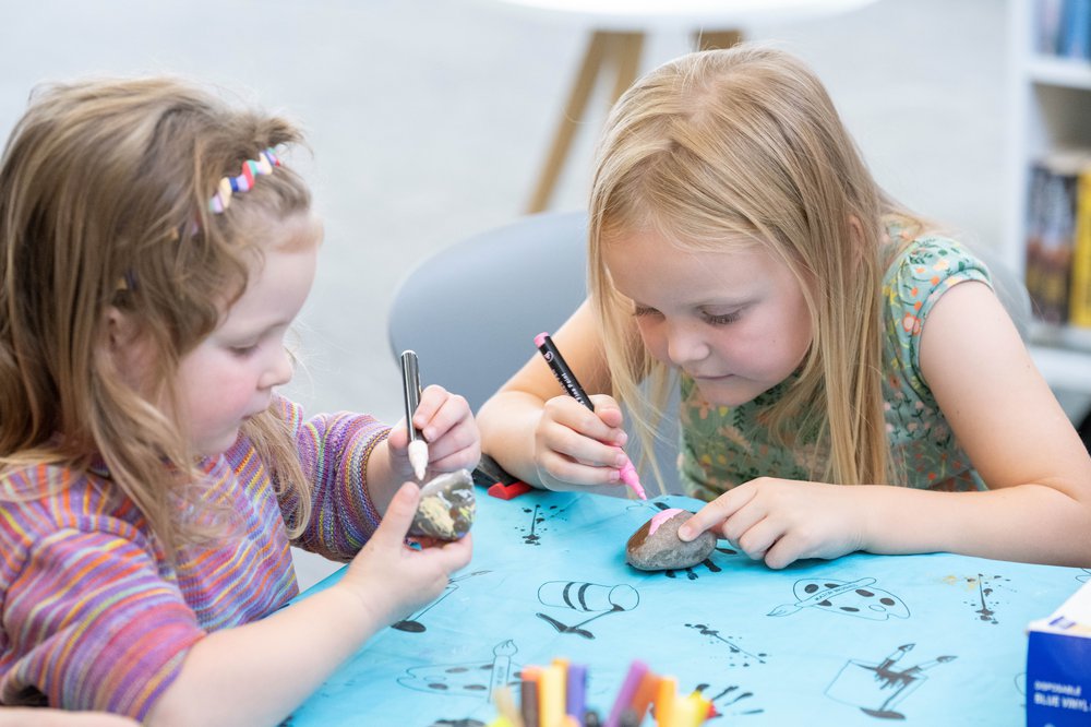 2 young girls decorating stones with different colours