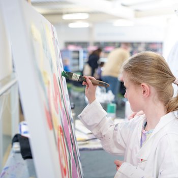 A girl painting on a canvas on an easel.