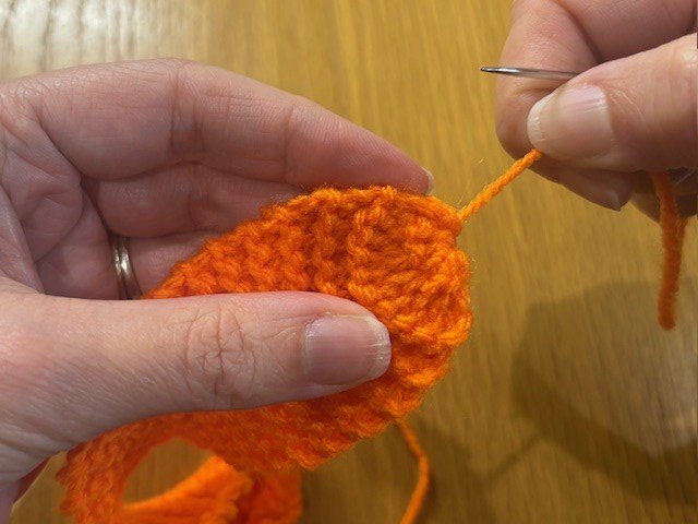 Pulling a stitched in yarn tail, to gather in the end of a piece of knitting