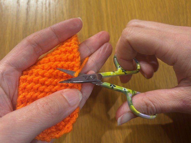 A pair of scissors snipping a yarn tail from a piece of knitting
