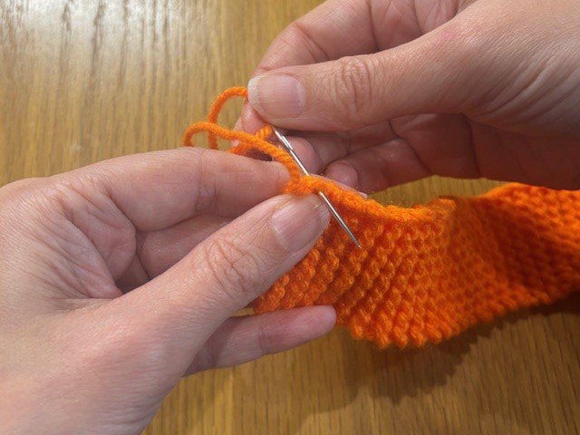 Stitching a wool tail along the side of a piece of knitting