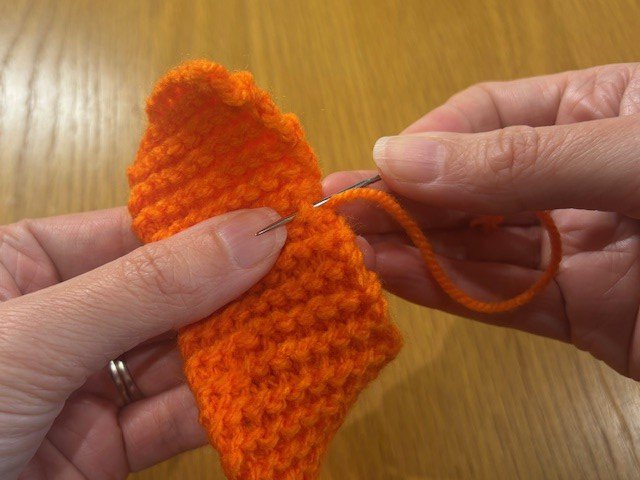 Stitching a yarn tail across the back of a knitting project