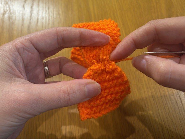 Pulling a stitched yarn tail on a knitting project, to created a gathered section