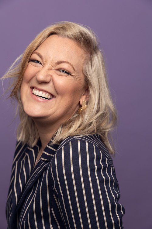 A headshot image of a woman laughing wearing a striped top