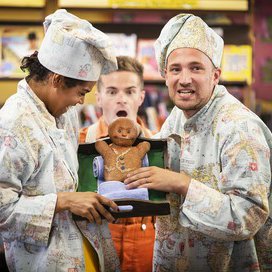 Two people dressed as chefs holding a gingerbread man.