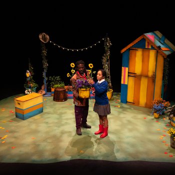 Schoolgirl Abi (Jazmine Wilkinson) and Grandad (Marcus Hercules) tend to a potted plant in the middle of a beautiful garden full of plants and a colourful shed.