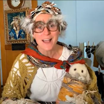 Female actor with large glasses with feathers, shawl and woollen hat holds Little Owl puppet