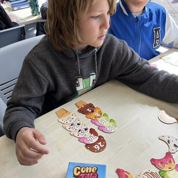 Two children play a game called Cone Zilla, featuring card pieces that look like ice cream and cones with numbers printed on them.