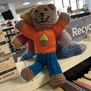 A hand knitted bear with and orange jumper