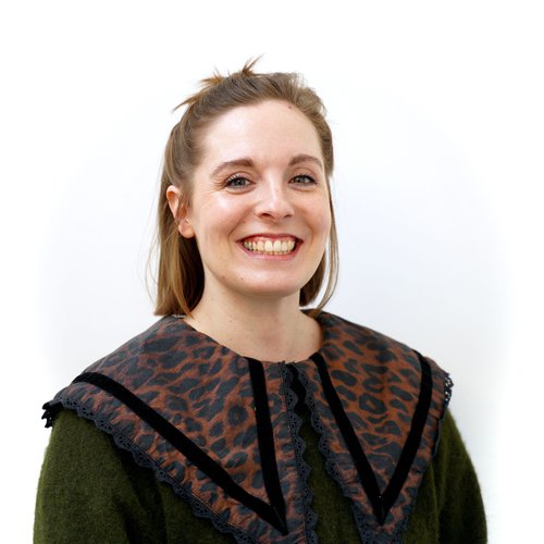 Female with short brown hair, smiling. Wearing a large brown and black leopard print collar over a green jumper against a white background