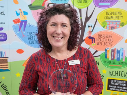 Helen Ackroyd who has dark hair and is wearing a red dress holding an award
