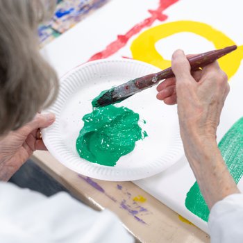 An elderly person is painting with bright green paint.