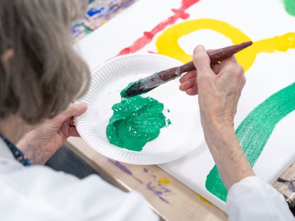 An elderly person is painting with bright green paint.