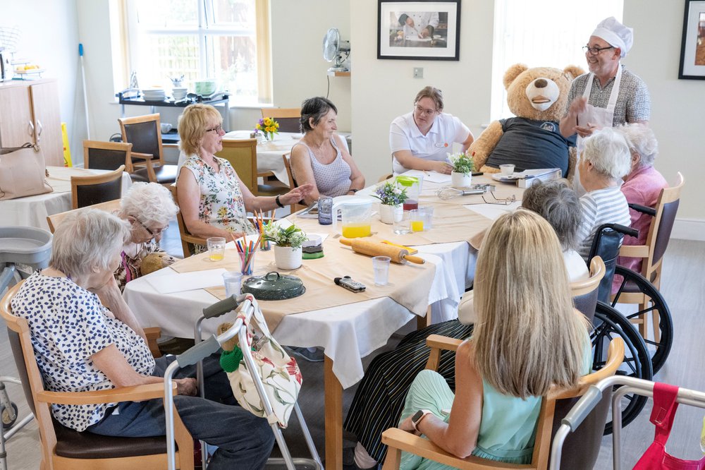 Care home residents sit around a long table, looking at Storyteller Andy Barrett.