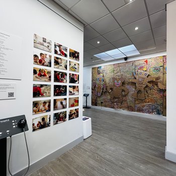 Exhibition wall featuring photographs of the school children, the audio frame, and large puppets in the background